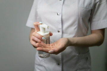 The girl is holding a liquid in a bottle. A doctor in a medical gown applies a disinfectant to his hands against bacteria and viruses. A nurse in white applies an antibacterial agent to her hands.