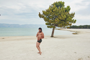 young man on the beach, young muscular man exercising on the beach, young muscular man doing bodibuilding exercises on the beach, athletic young man posing on the beach