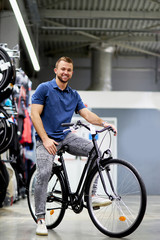 Fototapeta na wymiar portrait of young handsome guy sitting on new bicycle in sportswear store, going to buy, look at camera and smile