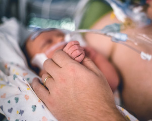 A man's hand holding a sleeping babies hand