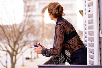 Attractive  yang woman in pajama is drinking coffee on balcony in the morning in city Paris. view...
