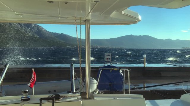 The view from a catamaran saloon on breaking waves about a pier in Korchula's port in a stormy weather, splashes, a strong wind blows into splashes on yachts, the Adriatic Sea, Croatia
