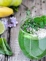 Spinach smoothie with fruits and seeds superfoods, decorated with mint leaves in a glass cup. Close-up, ingredients for smoothies on the table