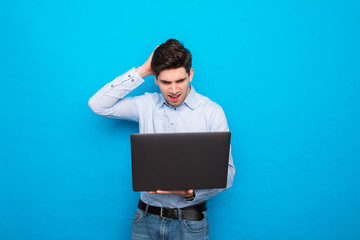Young confused man holding laptop isolated on blue background
