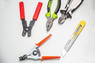 Tools for electrical installation on a white background. In the foreground a stripper for stripping wires. Tool for crimping wires, pliers, wire cutters, segment knife. Horizontal orientation.
