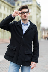 Young man with a smartphone in his hand, walking in the street. Young guy with modern hairstyle in urban background.