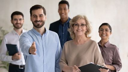Close up headshot portrait of two happy businessman shaking hand posture and mature businesswoman looking at camera. Diverse smiling employee standing behind of male and female company mentors.
