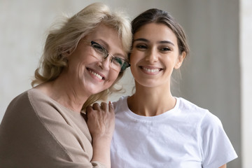 Close up headshot portrait picture of happy mature mother touching shoulder adult daughter enjoying tender moment looking at camera. Smiling woman and older mum hugging having fun together.
