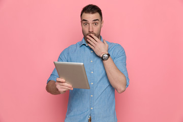 casual man holding his tablet and covering his mouth