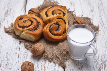 Basket of homemade buns with jam, served on old wooden table with walnuts and cup of milk