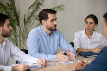 Confident businessman talking with female employee about finance project sit at table in boardroom at company meeting. Serious mentor discuss business strategy with colleagues during brainstorm.