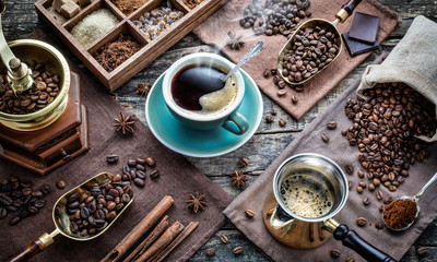 A cup of aromatic black coffee, a coffee grinder, a coffee maker, coffee beans of different varieties on the table. Morning espresso or Americano coffee for breakfast in a beautiful brown cup.