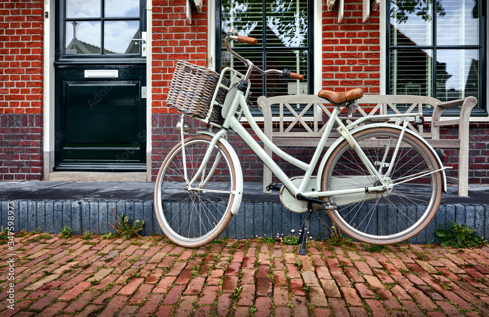 Wall mural volendam amsterdam netherlands. white retro bicycle with basket at street with brick red house and w