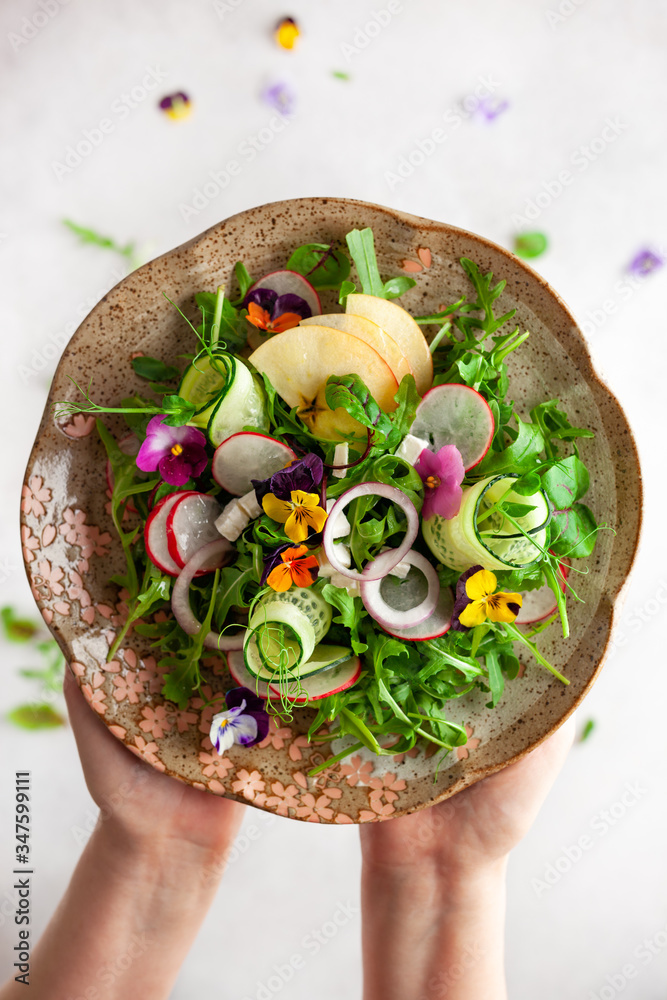 Wall mural delicious summer salad with edible flowers, vegetables, fruit, microgreens and cheese. woman holding