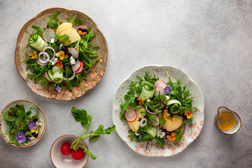 Delicious summer salad with edible flowers, vegetables, fruit, micro greens and cheese on a vintage grey background. Flat lay, top view, copy space.