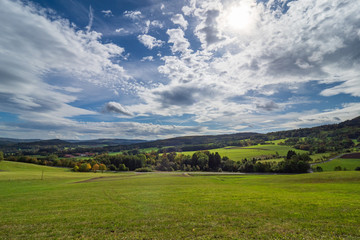 Fototapeta na wymiar Weitläufige Landschaft in der Rhön - Wiesen und Wald mit blauen Himmel und Wolken