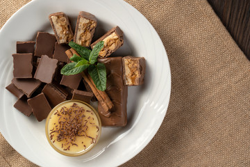 Plate with sweets: chocolate, sweets, honey, cinnamon and mint on a natural background. The concept of relaxation, eating.