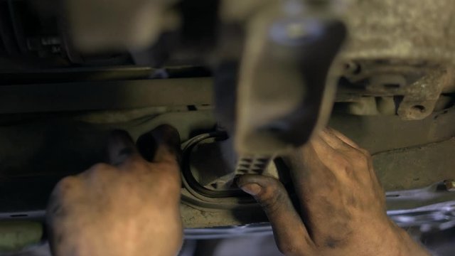 Close up unscrewing car part. Dirty mechanic worker's hands are uninstalling old car detail.