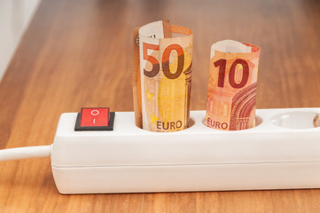 Euro banknotes inserted into an extension socket on a wooden surface. Expensive concepts of energy...