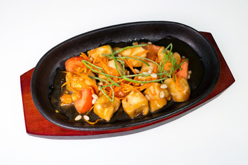 Baked fish slices in a roasting pan with fresh vegetables on a wooden plate on a white background