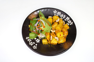 Vegetarian dish of baked apples with cashews and lettuce, young cabbage and onion rings on a black plate on a white background