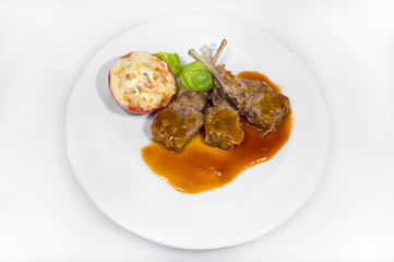Lamb ribs with sauce and stuffed tomato with cheese and mushrooms on a white plate on a white plate