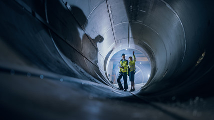 Two Heavy Industry Engineers Walking Inside Pipe, Use Laptop, Have Discussion, Checking Design....