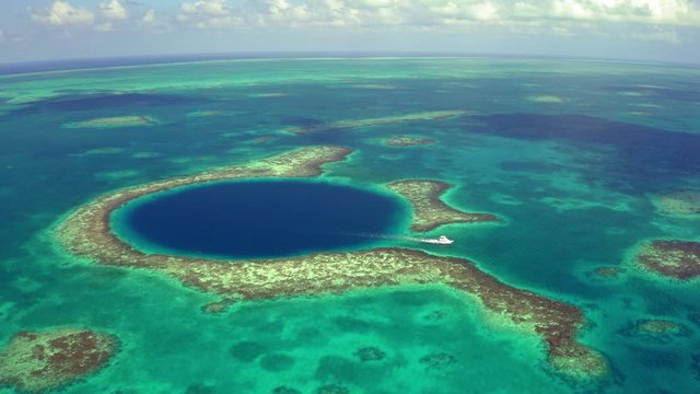 Aerial view of yacht moving out from marine sinkhole, drone approaching seascape against cloudy sky - Great Blue Hole, Belize