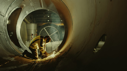 Professional Heavy Industry Welder Working Inside Pipe, Wears Helmet and Starts Welding. Construction of the Oil, Natural Gas and Fuels Transport Pipeline. Shot with Warm Light.