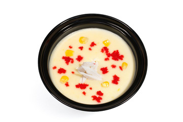Mashed soup garnished with Tobiko, grains of corn and cheese in a black deep plate on a white background