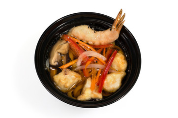 Seafood soup fish slices and shrimp in the dough, mushrooms and vegetables in a deep black plate on a white background