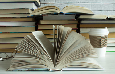 Clutter on the table - a lot of open and closed books close-up and a paper Cup of coffee with a lid