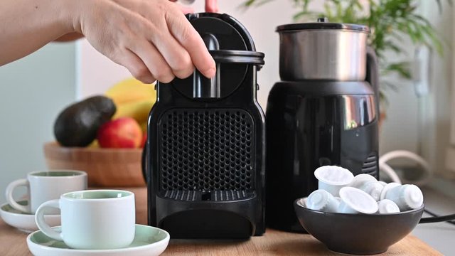 Woman pressing a button on a coffee maker and making espresso. Conceptual modern coffee machine at home, on a table with fruits and a cup of fresh aromatic drink. Copy space