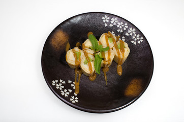 Sweet pancake rolls with banana, kiwi and apple poured with sweet syrup on a black round plate on a white background