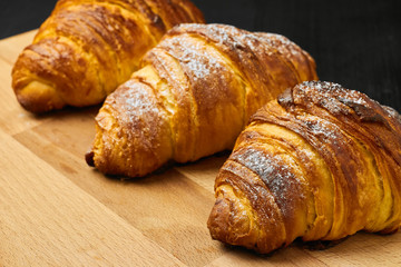 Three croissants with sugar powder on a wooden desk on a black background. Homemade baking concept.