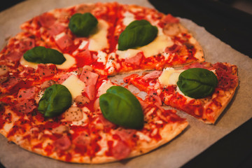 Close up. A home made pizza in the oven with prosciutto, tomato, mushrooms, cheese and basil. Traditional Italian food made from fresh bio ingredients by locals at home. Rome, Lazio, Italy.