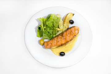 Fried piece of salmon with mashed potatoes and lettuce leaves decorated with olives and lemon idol on a white plate on a white plate
