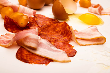 Broken chicken egg, slices of sausage and bacon and tomatoes on a white background. Close up.