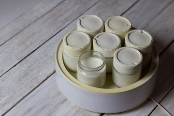 Homemade yogurt in glass jars in electric device on white wooden background