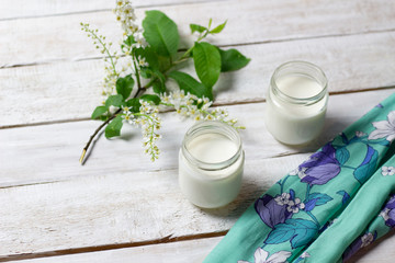 Obraz na płótnie Canvas Home made yogurt in glass jars on textile cover on white wooden background with bird cherry branch