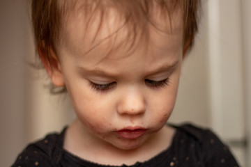 Close-up portrait of a little cute white baby with a dirty face in soft light and blurry background