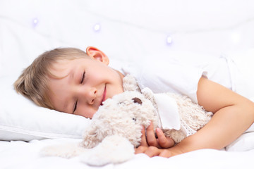 Obraz na płótnie Canvas Charming little white boy sleeps in bed. hugs a soft toy