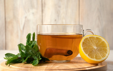 Transparent Cup with fragrant black tea, mint and cinnamon, on a Board on a natural light background. Concept for your design, advertising.