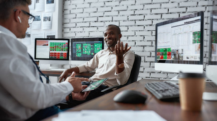 Get a Big Jump. Two diverse colleagues traders discussing ideas while sitting in the office in front of multiple computer screens.