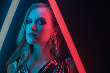 Fashion portrait of beautiful woman posing in colorful bright neon uv blue and red lights. Model wearing luxury earrings. Copy, empty space for text