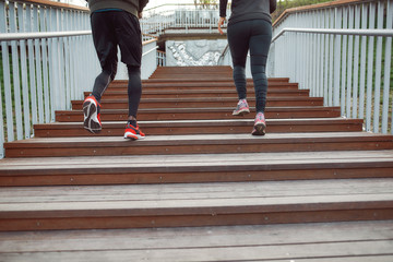 Run. Cropped view of a couple in black sportswear running up stairs outdoors. People jogging in the morning. Healthy people