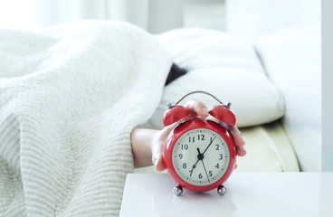 young woman sleeping on bed pressing snooze button on black vintage alarm clock at seven o'clock morning in bed room at home, lifestyle, good morning, healthy sleep and joyful weekend concept