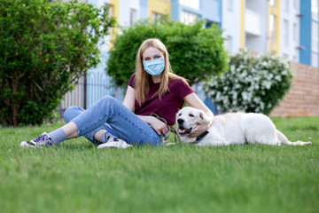 Coronavirus pandemic. girl in a protective mask walks a dog in a summer park, a woman with a puppy in quarantine