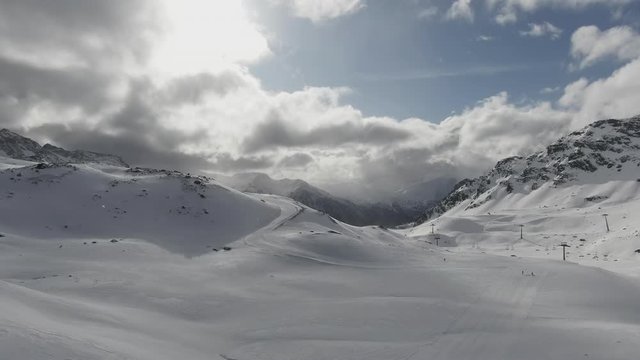 Winding trail through rugged snow covered mountain peaks in winter with the sun peeping through the clouds in a blue sky