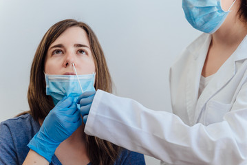 Female doctor in a protective suit taking a nasal swab from a person to test for possible...
